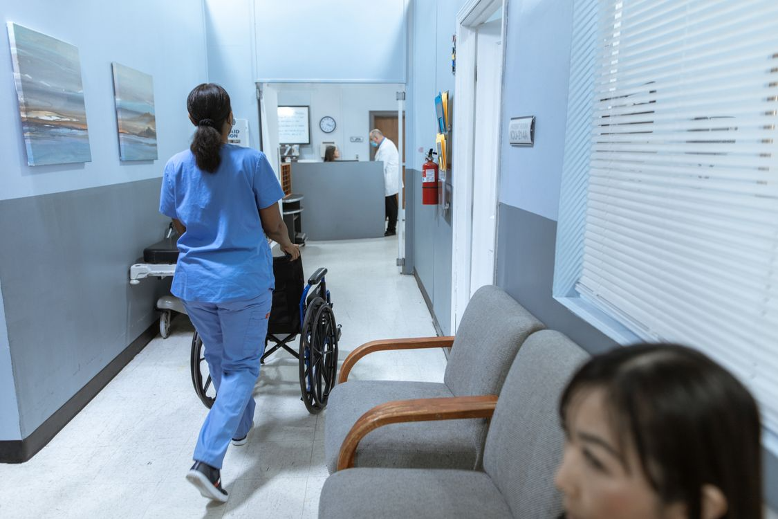 Care team member walking a wheelchair down a hospital corridor